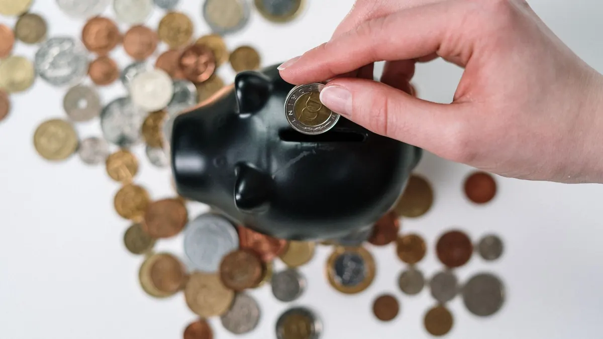 Hand stopt een munt in een zwarte spaarpot tussen verspreide munten