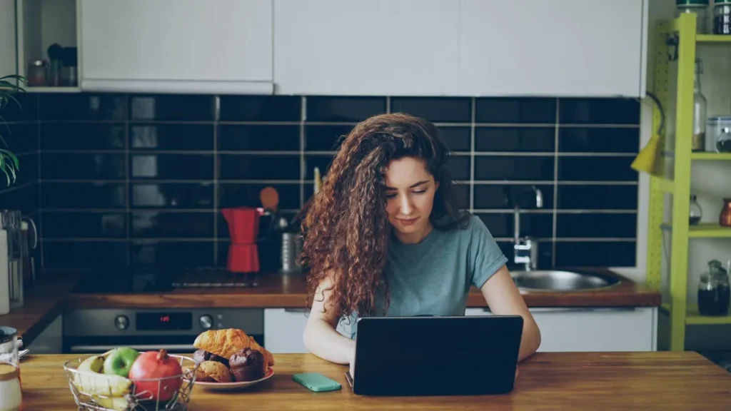 Vrouw werkt op een laptop aan de keukentafel en verdient geld vanuit huis