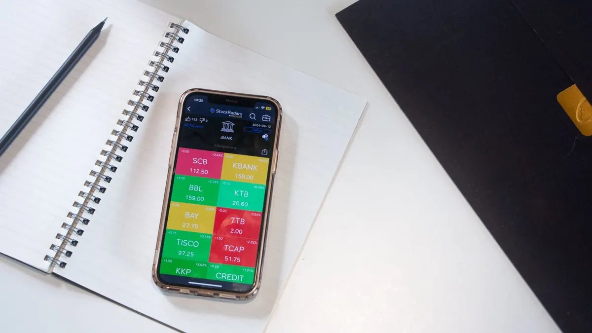 Smartphone met beleggingsapp naast een notitieboek op een wit bureau
