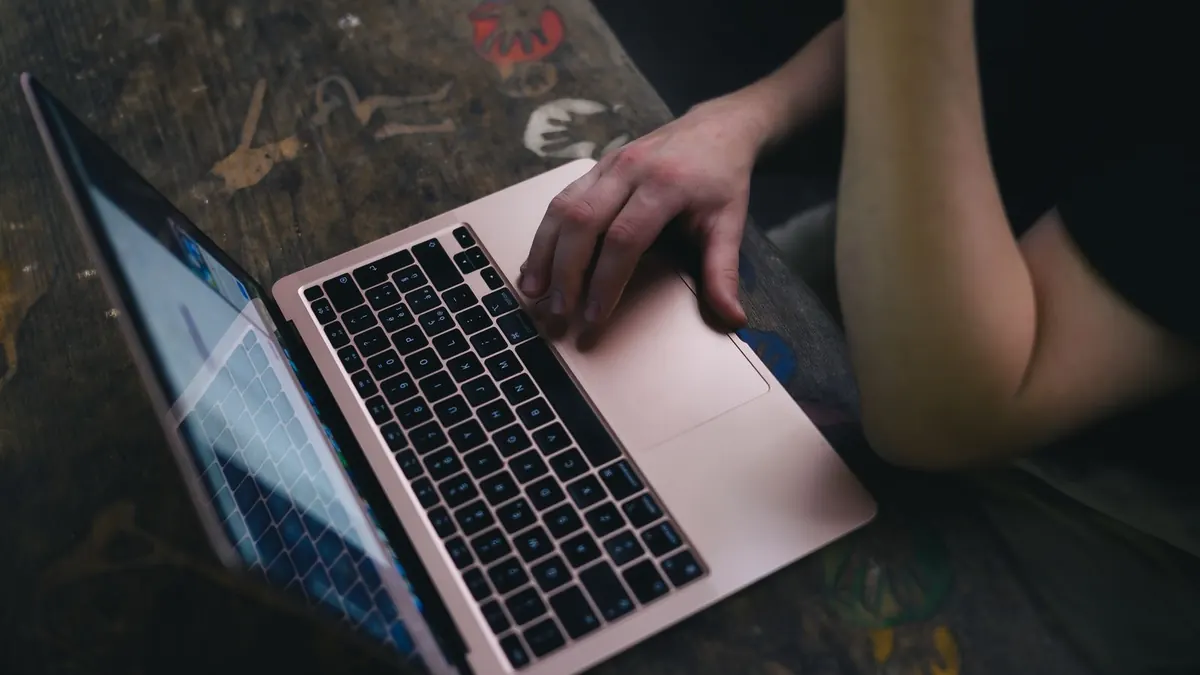 Iemand werkt 's avonds op een laptop aan een houten tafel, bijverdienen naast je baan