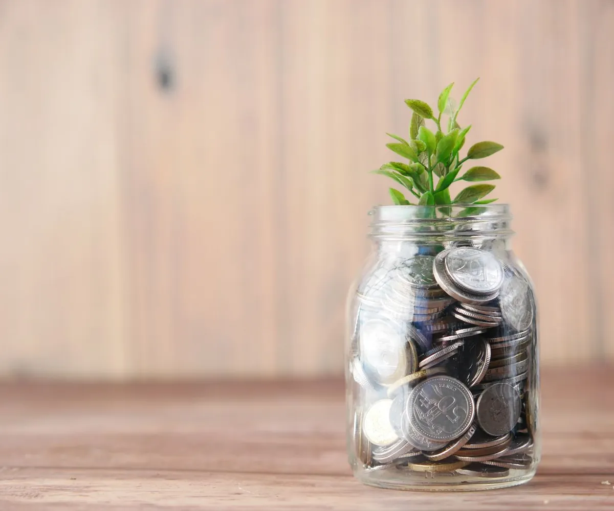 Glazen spaarpot vol munten met een groeiende plant als symbool voor sparen