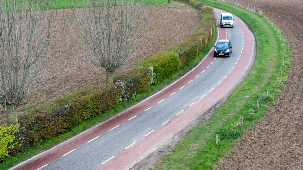 Twee auto's rijden over een bochtige weg door akkers, voorbeeld van verplichte WA-verzekering