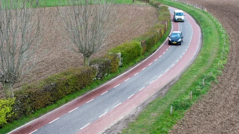 Twee auto's rijden over een bochtige weg door akkers, voorbeeld van verplichte WA-verzekering